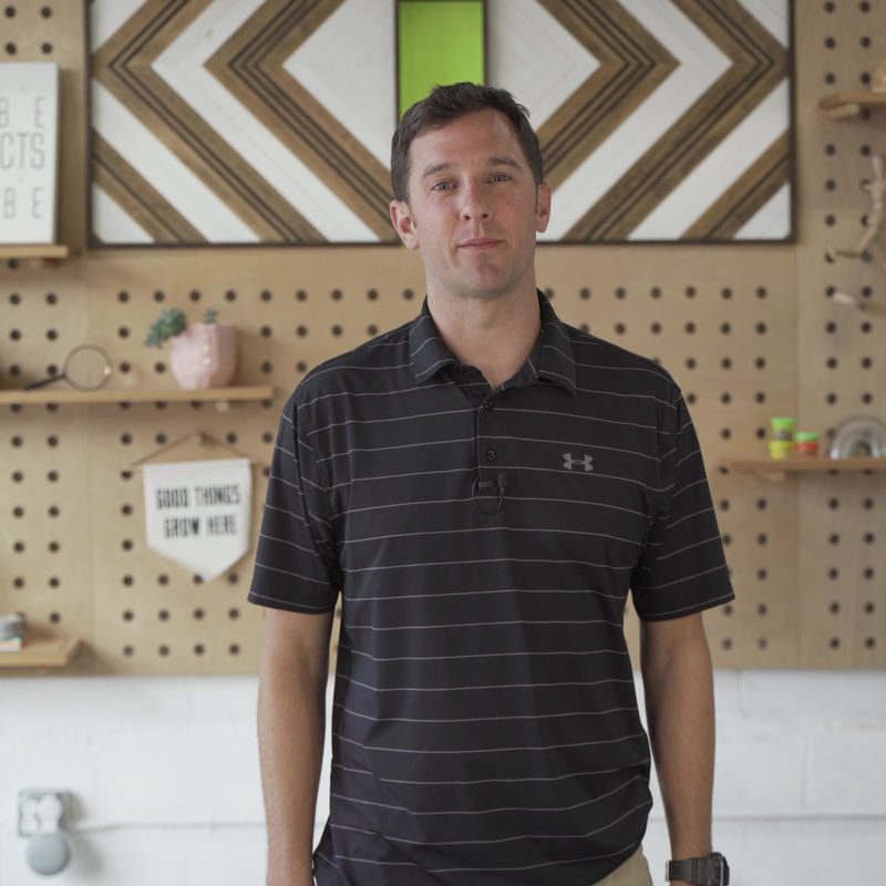 John Hawley headshot in a striped polo in front of a pegboard wall
